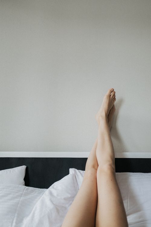 Free Minimalist photo of bare legs crossed at the ankle on a bed with white pillows. Stock Photo