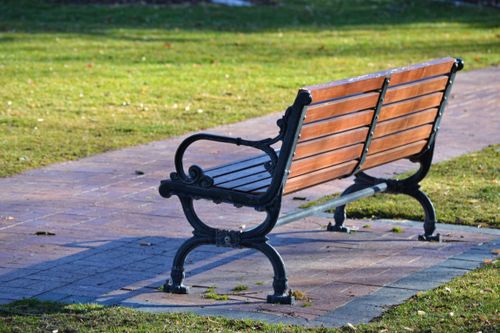 Free A picturesque vintage wooden bench in a sunny park with a paved pathway. Stock Photo