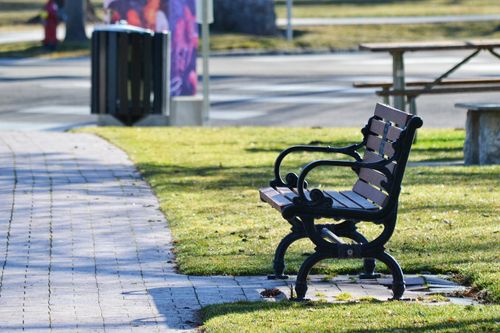 Free A solitary wooden bench on a sunlit pathway in an urban park setting, offering tranquility. Stock Photo