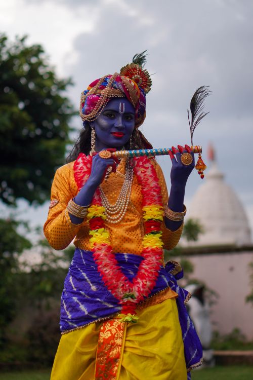Free Woman dressed as Krishna in vibrant costume with flute at cultural festival. Stock Photo