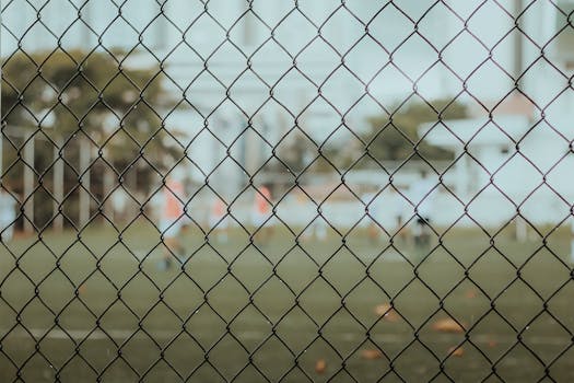 A soccer field viewed through a chain link fence with players in the background.