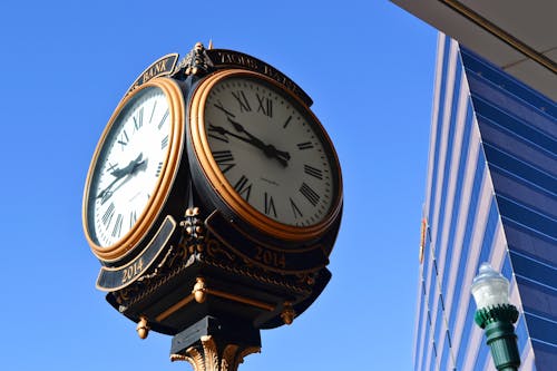 Close-up Photo of Street Clock Near Tall Building