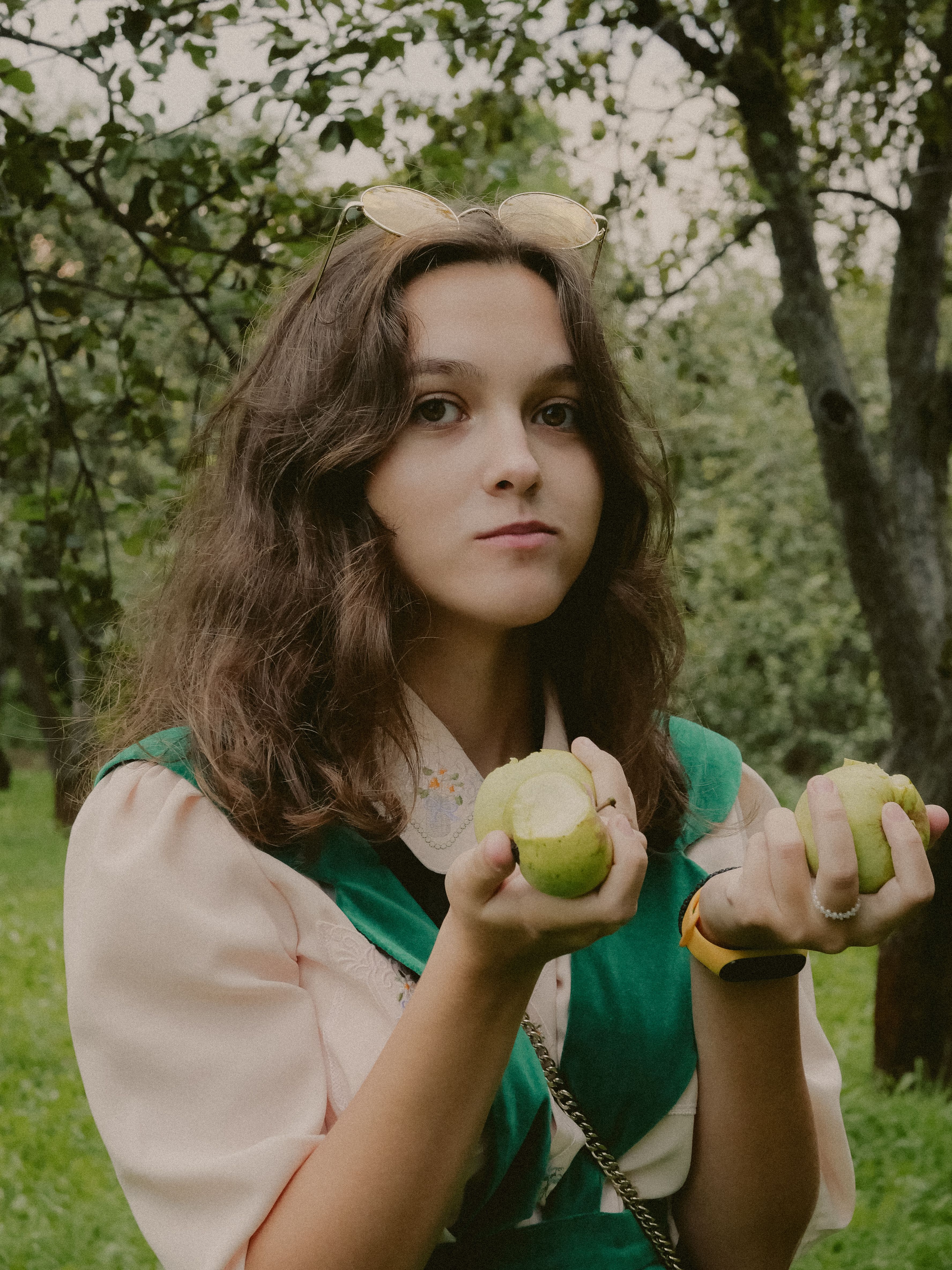 Brunette woman in vintage outfit holding green apples in a lush orchard.
