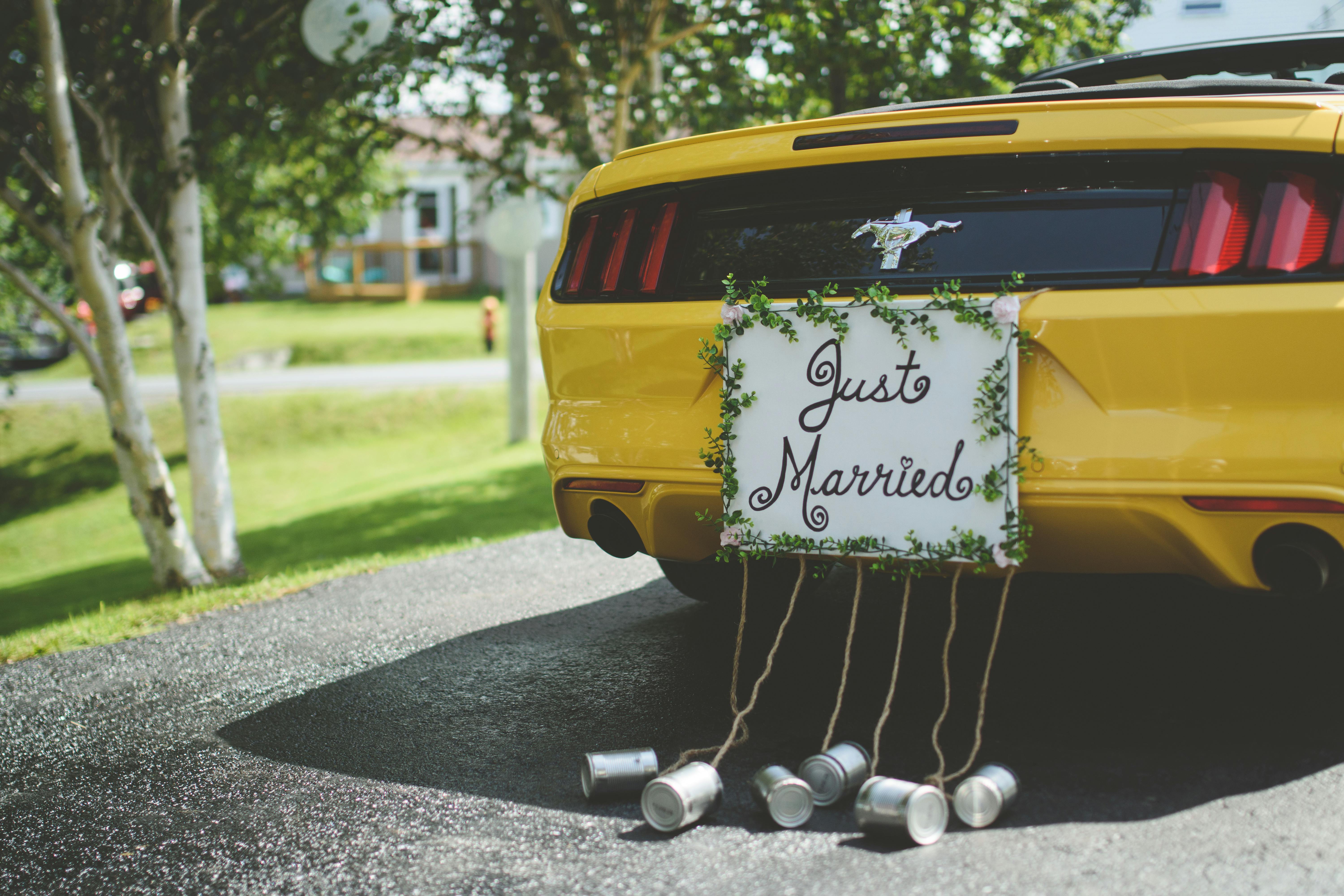 A vibrant yellow sportscar adorned with a Just Married sign and tin cans on a sunny day.