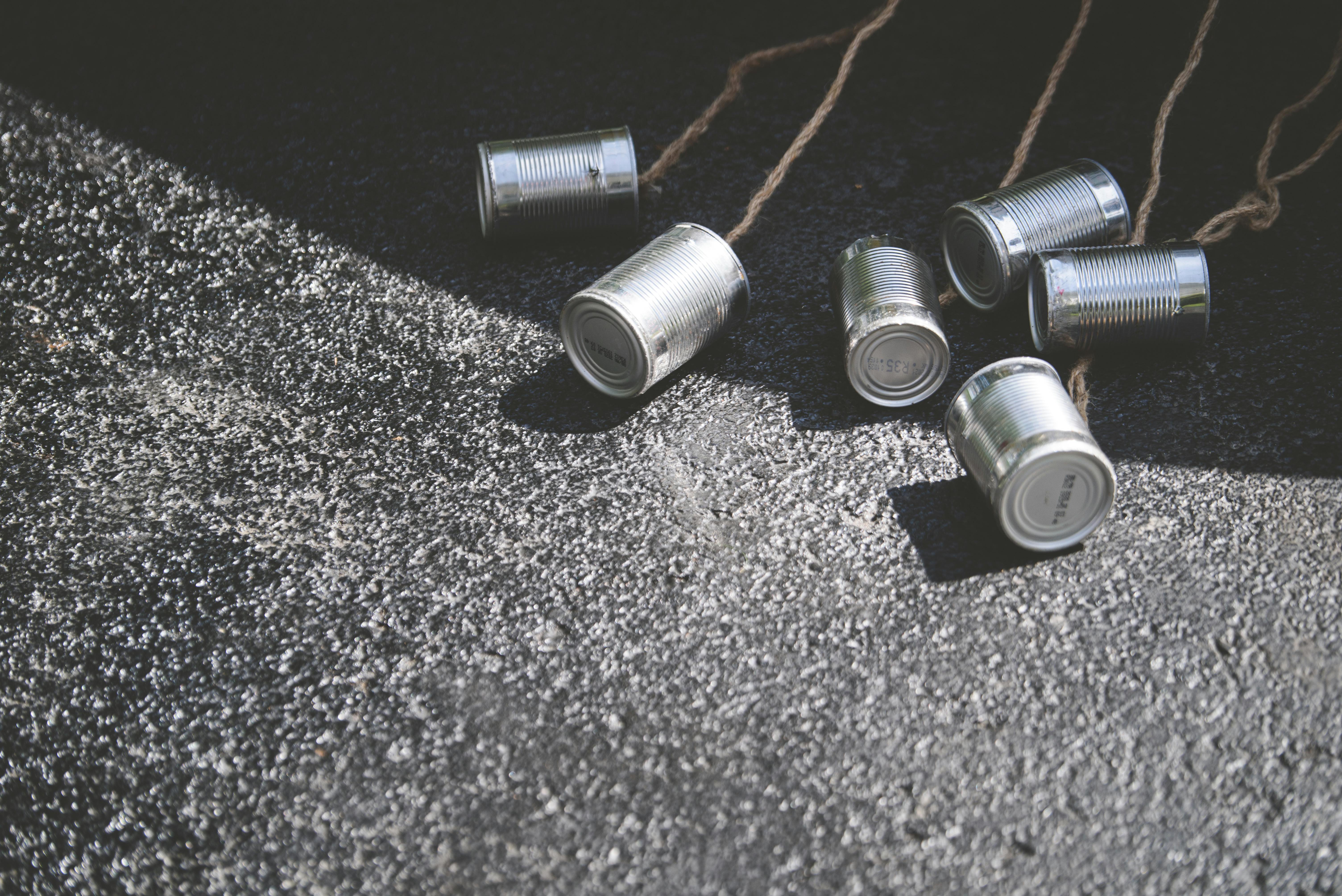 Tin cans tied with ropes placed on asphalt, creating street texture.