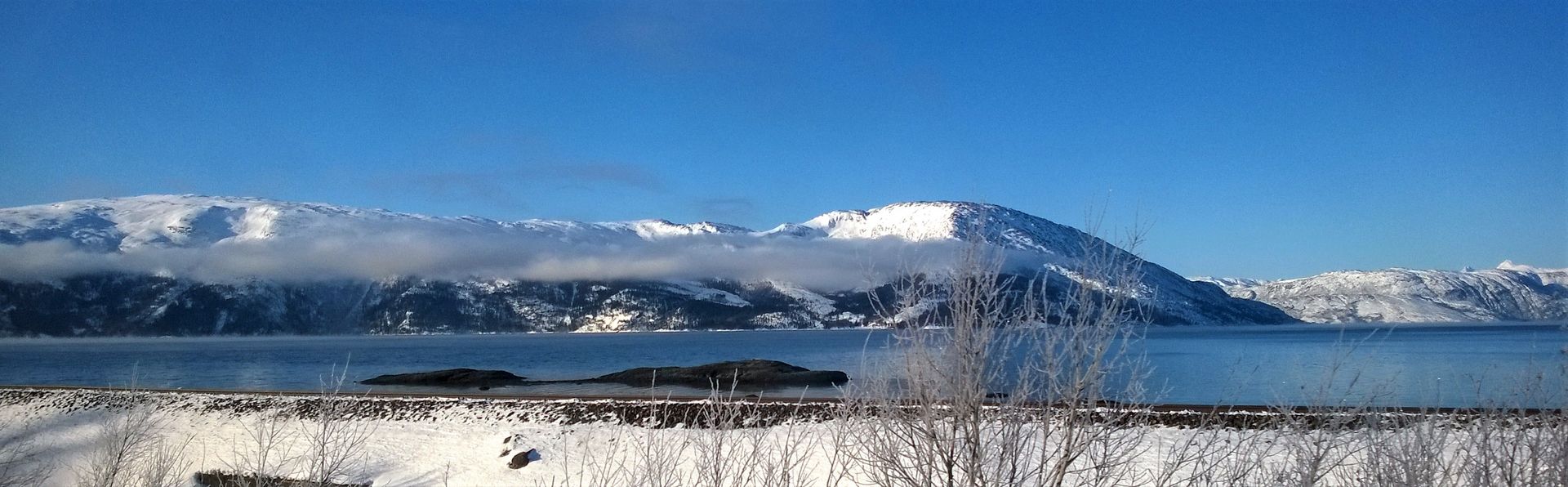 Snowy Norwegian mountains and frozen lake under pale winter sky — frosty, cold, still