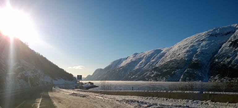 A stunning winter landscape in Vefsn, Nordland, Norway, showcasing snow-covered mountains and a serene roadway.