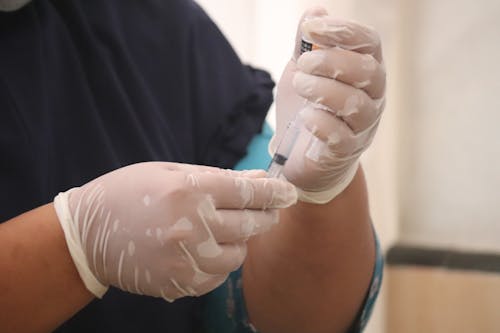 Person in Black Scrubs and White Latex Gloves Holding Syringe
