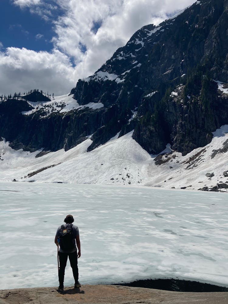 Man By Frozen Lake In Mountains