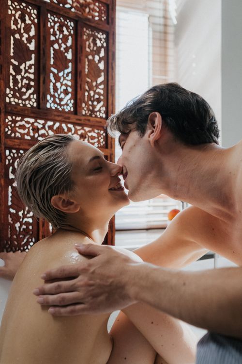 Free A couple sharing a loving kiss in an intimate indoor setting, backlit by natural light. Stock Photo