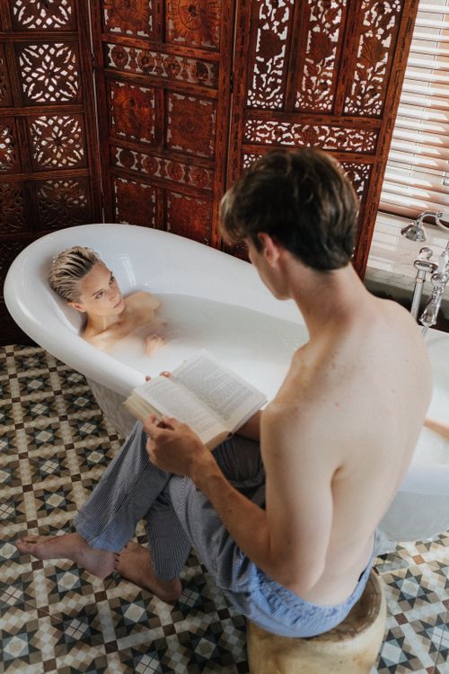 Free Couple enjoying a relaxing bath with a book in a cozy, intimate bathroom setting. Stock Photo