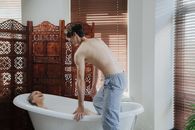 Topless Man in Blue Denim Jeans Standing on Bathtub