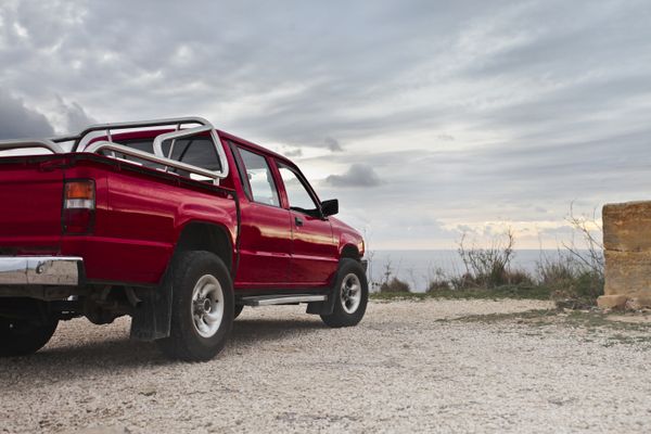 Red pickup truck parked on gravel by a cloudy coastline — photo by Andrea Piacquadio on Pexels