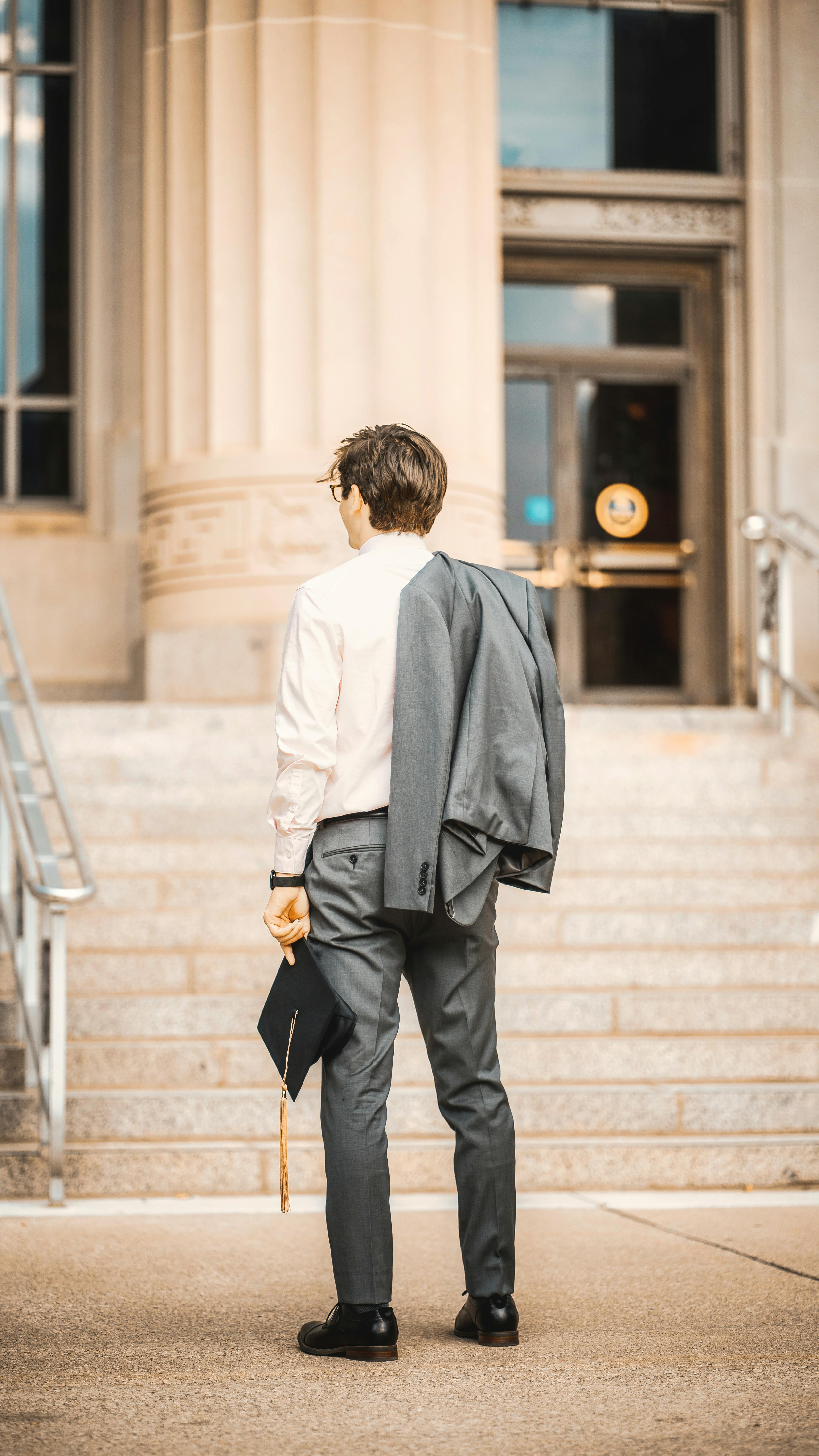 A young graduate in formal attire standing on the steps of a university building.