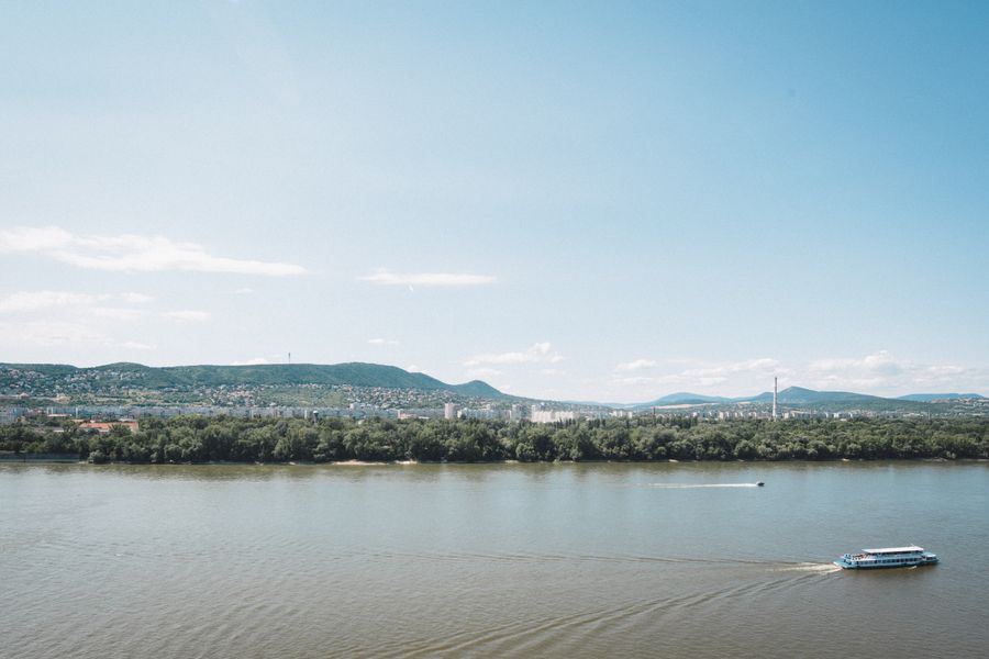 Wide view of the Danube with Buda's green hills and the Pest skyline beyond, showing how the river divides Budapest