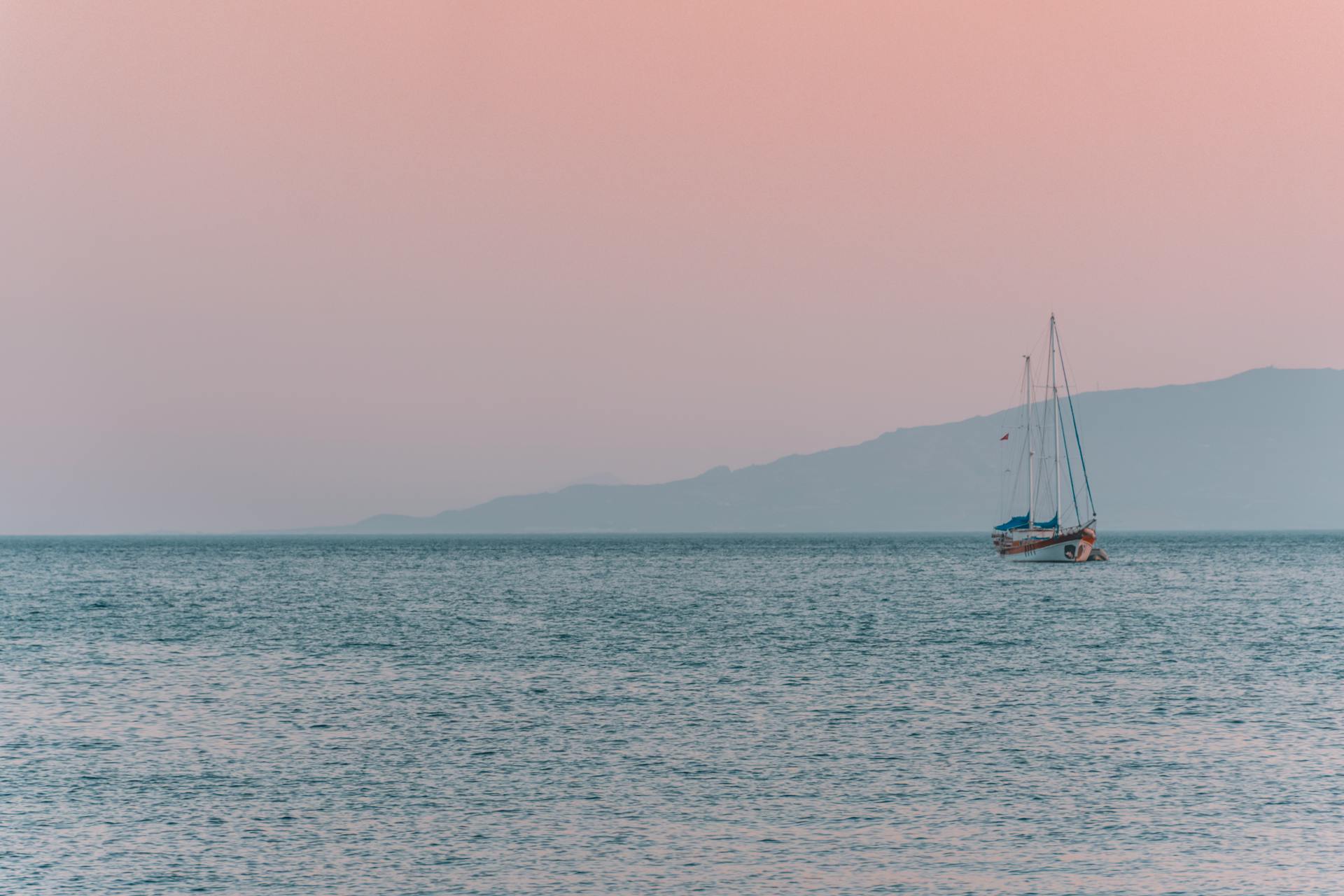 A peaceful sailboat drifts on calm waters during a stunning Turkey sunset.