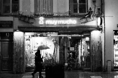 Grayscale Photo of a Person Walking on the Street while Holding an Umbrella