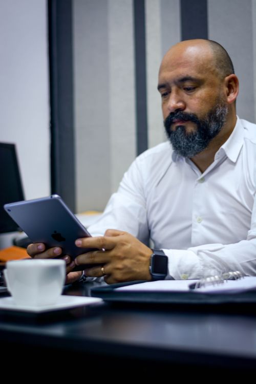 Free Bearded man in white shirt using digital tablet at a desk with a coffee cup nearby. Stock Photo