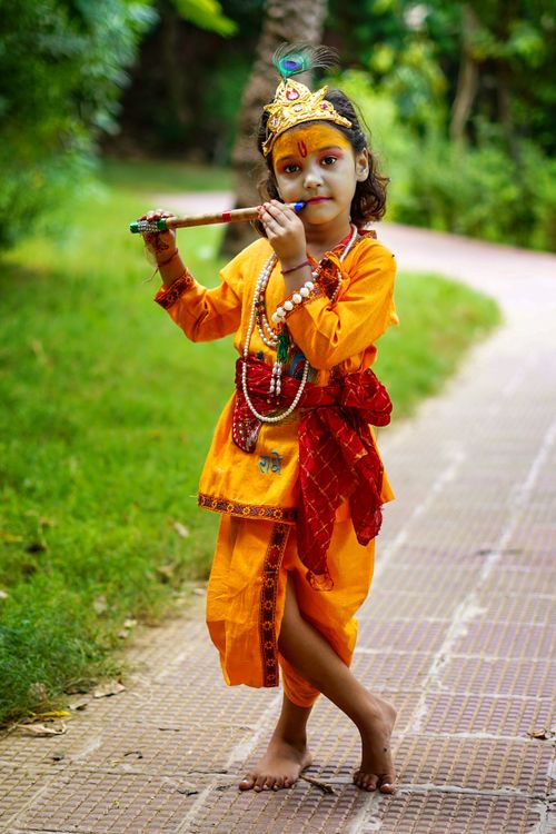 Free A young child dressed in traditional attire plays a flute outdoors on a path. Stock Photo