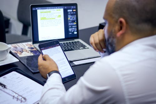 Man in White Dress Shirt Using a Tablet and a Laptop