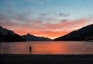 在宁静的湖面上，一个人矗立在令人惊叹的日落映衬下，远处有山脉