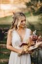 一位穿着优雅礼服的微笑新娘在户外自然光下捧着花束