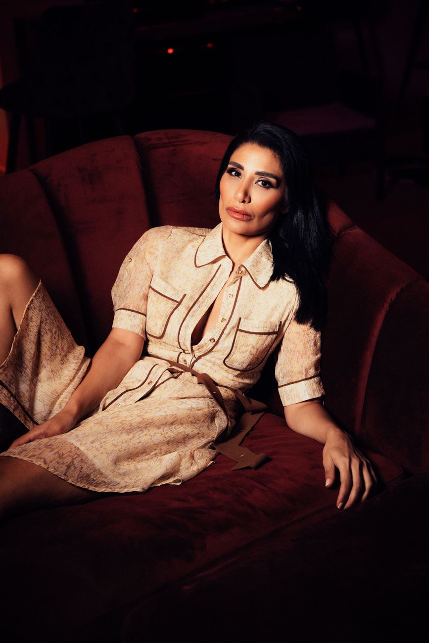Elegant woman in a stylish dress lounging on a plush red sofa, exuding modern luxury.
