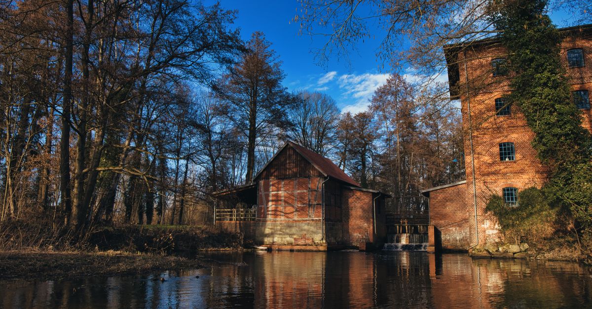 Beautiful historic brick mill by a serene river in Faßberg, Germany, surrounded by trees.