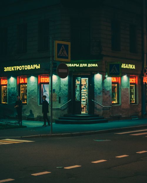 Free A moody nighttime street scene featuring people walking past a store with vibrant neon lights. Stock Photo