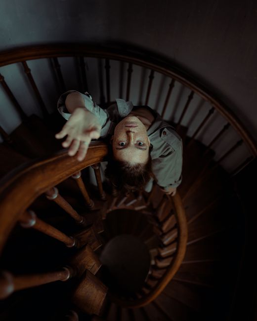 A woman reaching out dramatically on an elegant spiral staircase, gazing upwards.