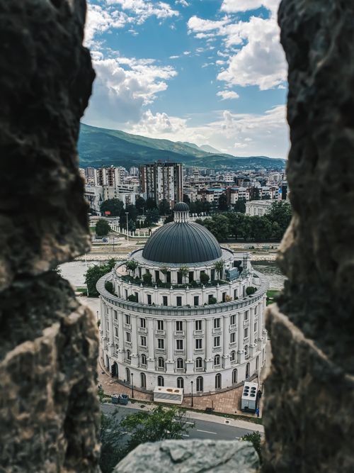 Free A captivating view of the rotunda in Skopje, framed by ancient stone architecture against a vibrant cityscape. Stock Photo