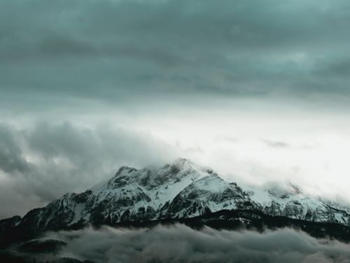 Free Stunning view of snow-covered mountain peaks engulfed by swirling clouds under a dramatic sky. Stock Photo