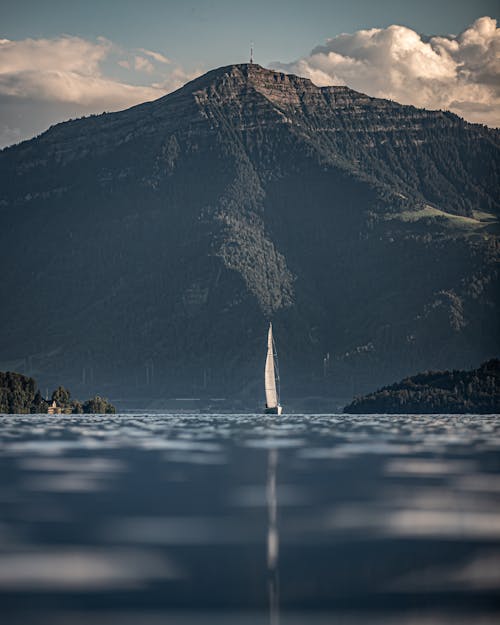 White Sailboat on Body of Water Near Mountain