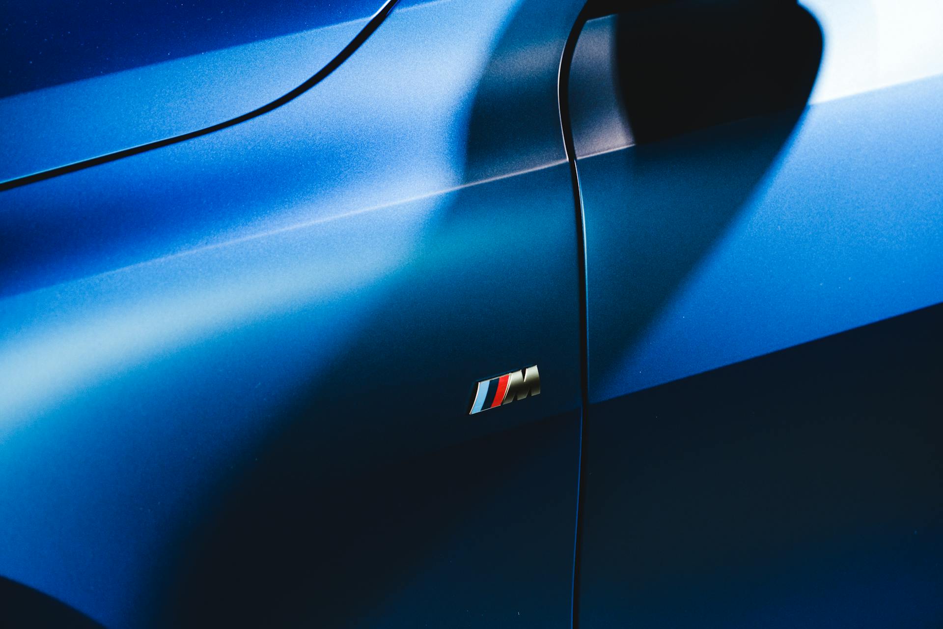 Close-up of a sleek blue car door with a prominent shadow and logo.