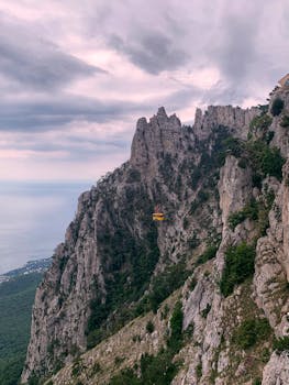 Scenic view of a cable car against dramatic rocky cliffs in Crimea, under a cloudy sky.