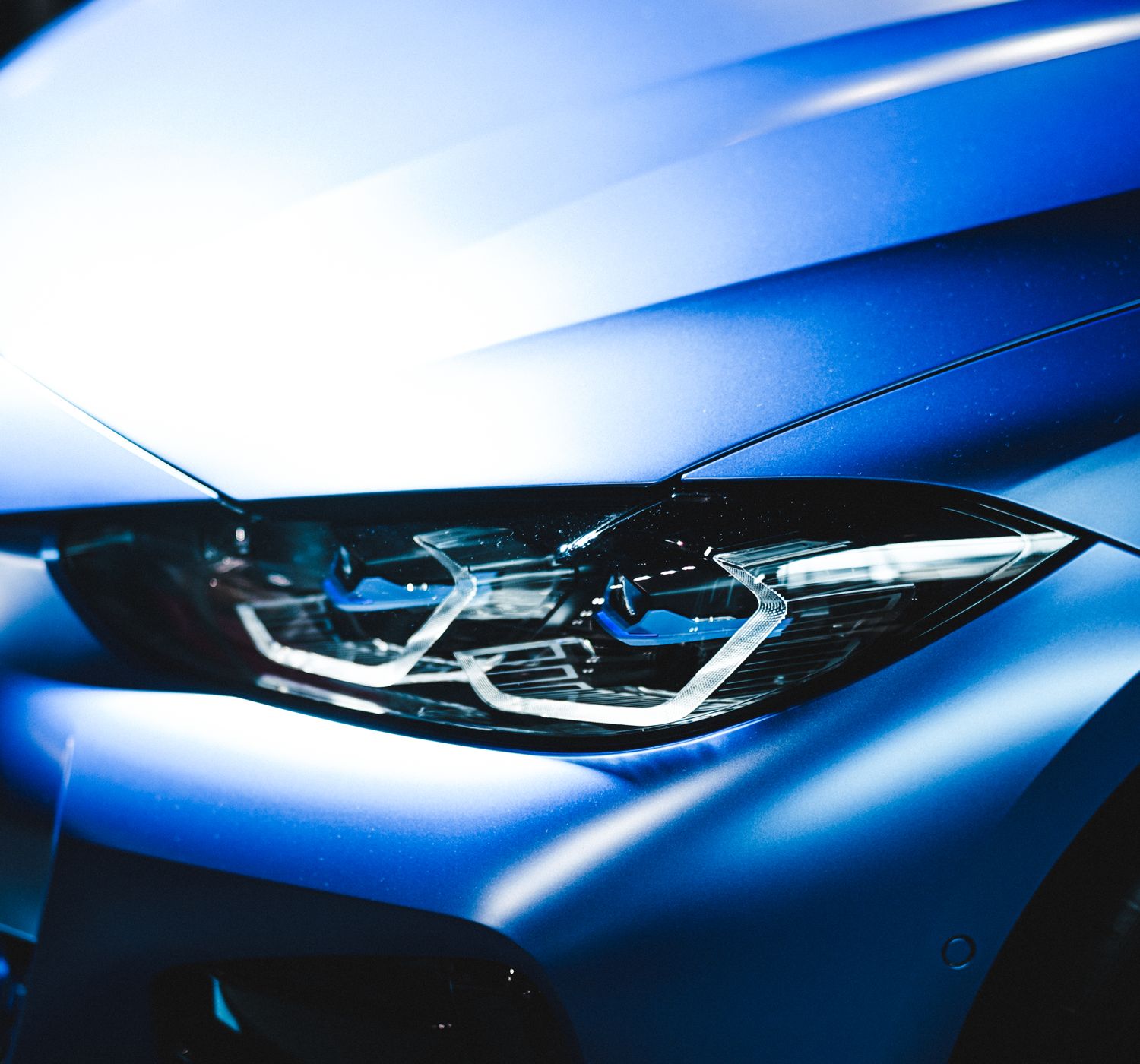 Detailed view of a sleek blue car focus on the headlight, emphasizing modern design.