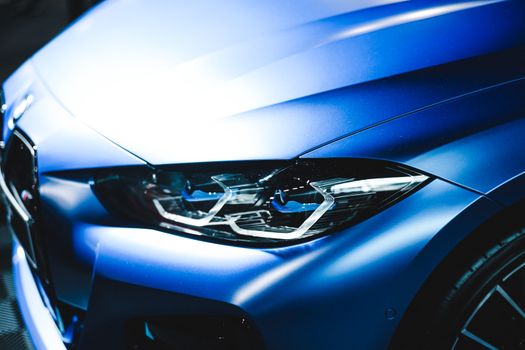 Detailed view of a sleek blue car focus on the headlight, emphasizing modern design.