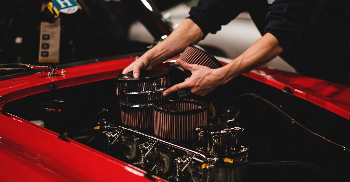 Close-up of a mechanic installing air filters on a classic red car's engine inside a garage.
