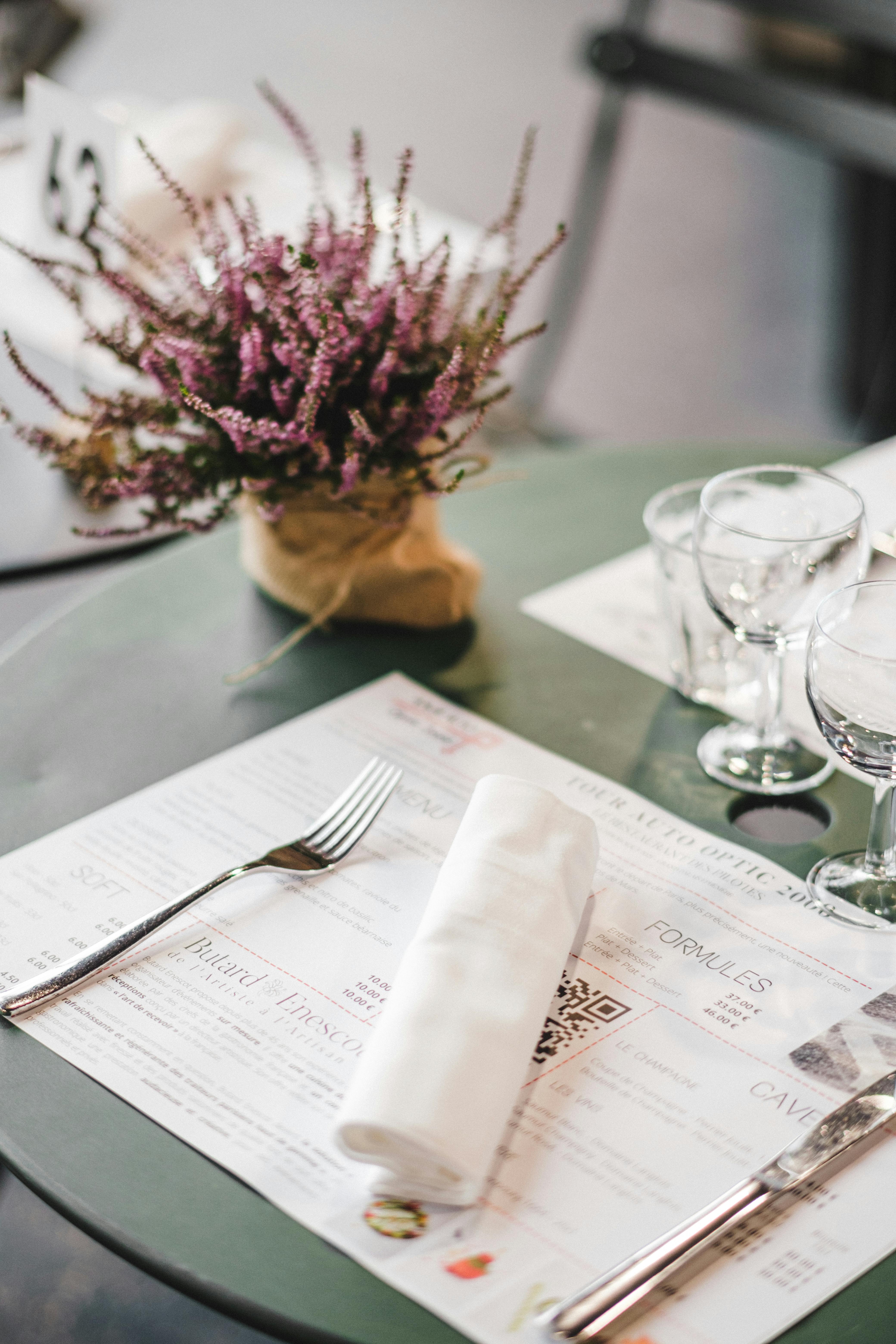 A stylish table setup in a restaurant featuring a menu, cutlery, and decorative flowers.
