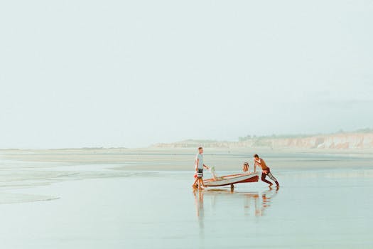 Two men pushing a small boat on the tranquil beach of Canoa Quebrada, Brazil.