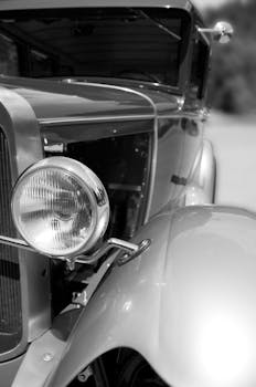 Detailed close-up of a vintage car's headlight and fender in black and white.
