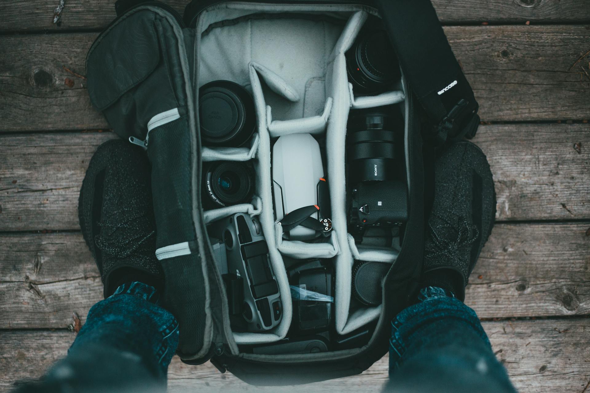 Flat lay of camera gear in a backpack on wooden background.