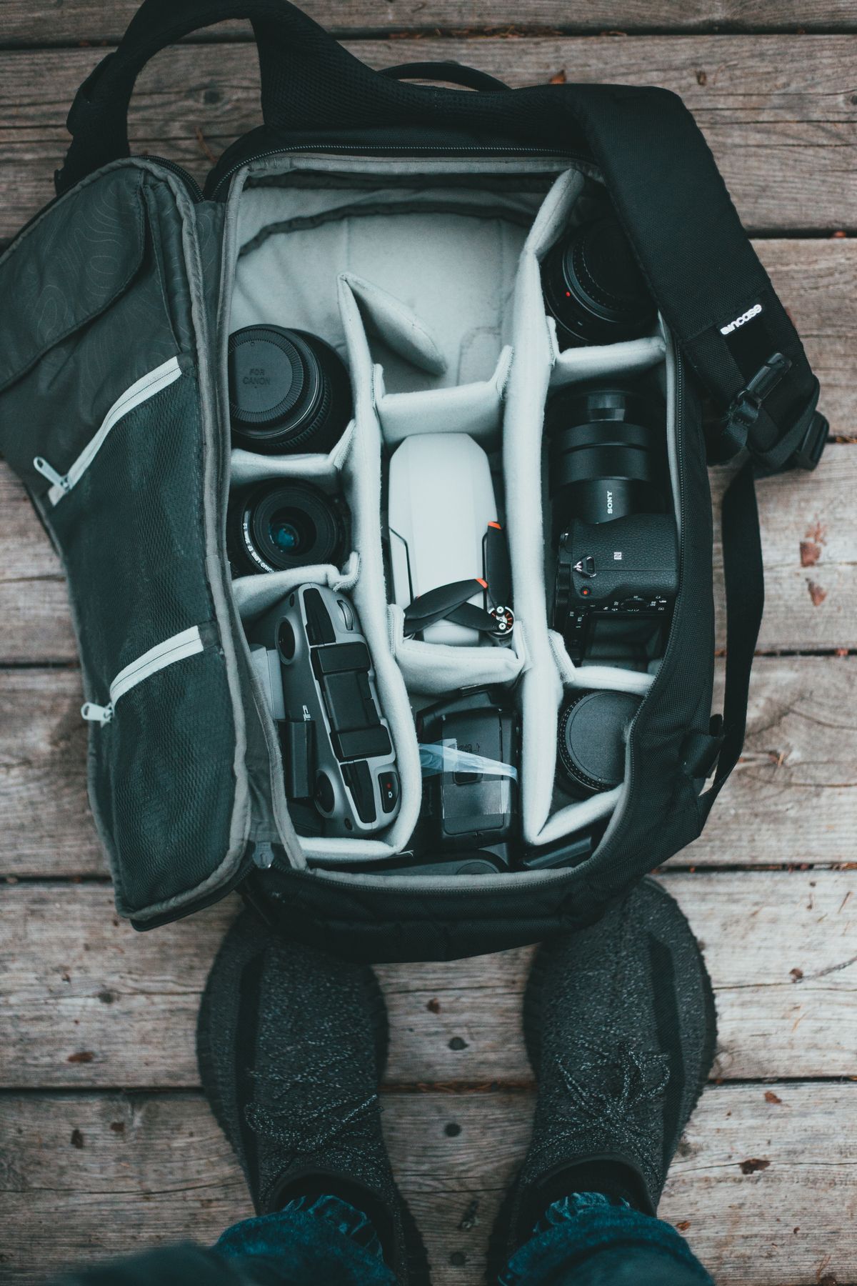 Organized travel gear bag laid flat with electronics and accessories separated into sections on a wooden floor