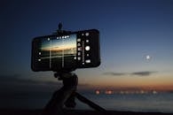 在一个夜晚，智能手机被架在三脚架上拍摄海上的日落