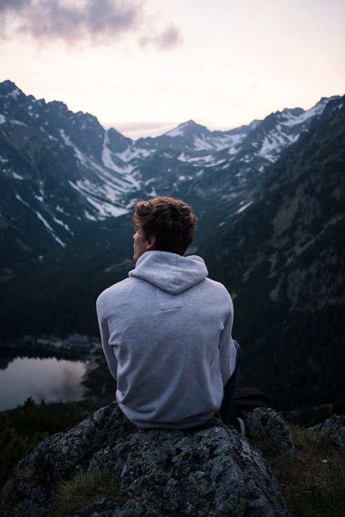 男人穿着白色连帽衫坐在一块岩石上，山上的景色