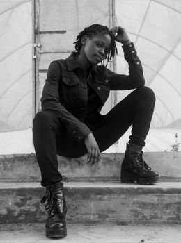 Black and white portrait of a stylish woman in boots sitting on stairs with a confident pose.