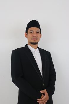 A confident man wearing a kufi and suit jacket, posing in front of a plain background. - Fotografer Sidoarjo