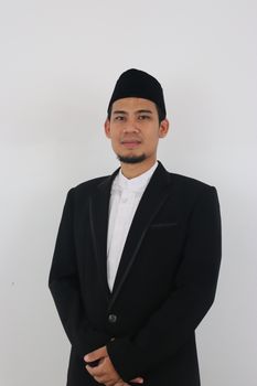 Portrait of a man in a black suit with traditional headwear on a white background. - Fotografer Sidoarjo
