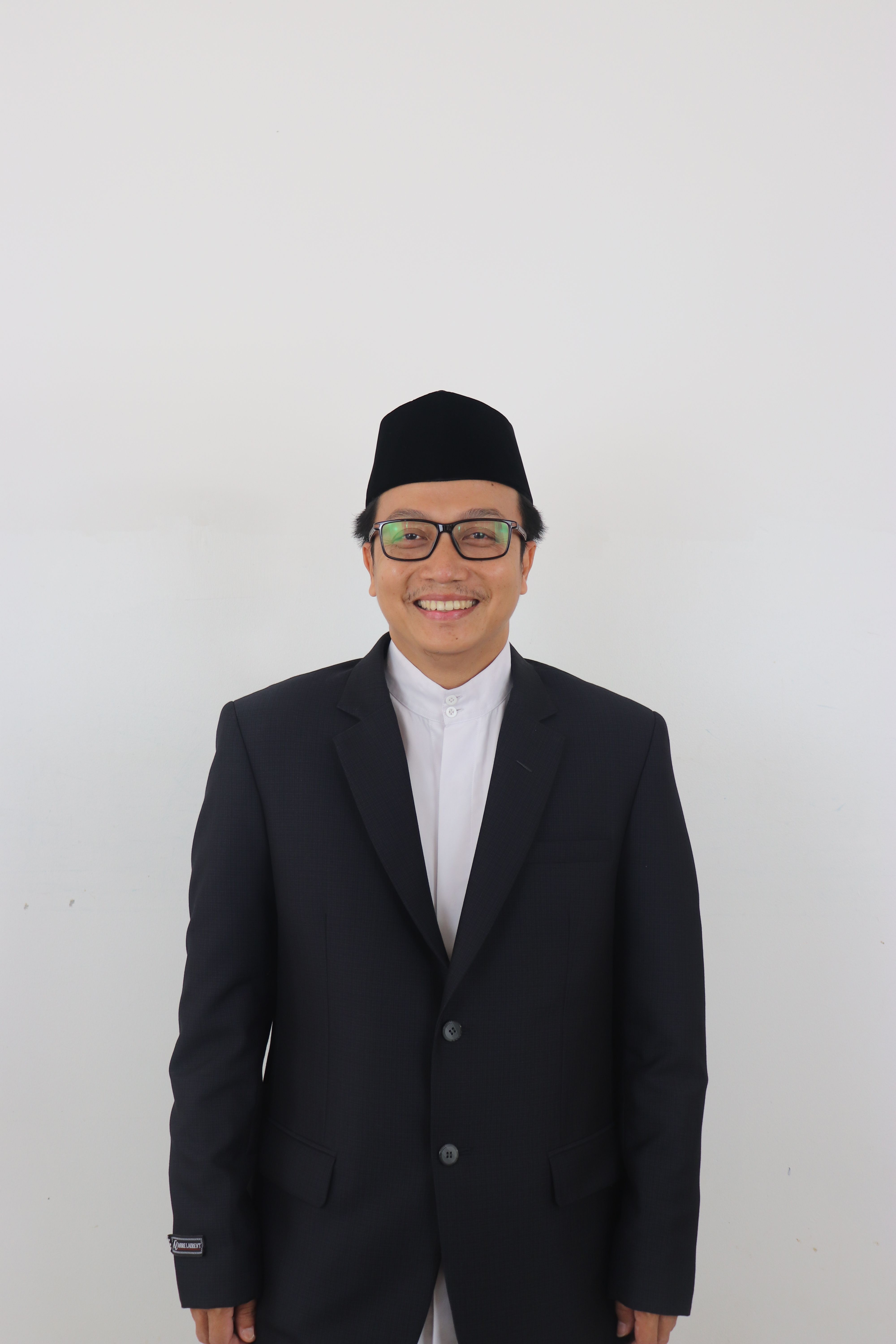 Portrait of a smiling man in a black suit and traditional hat on a white background.