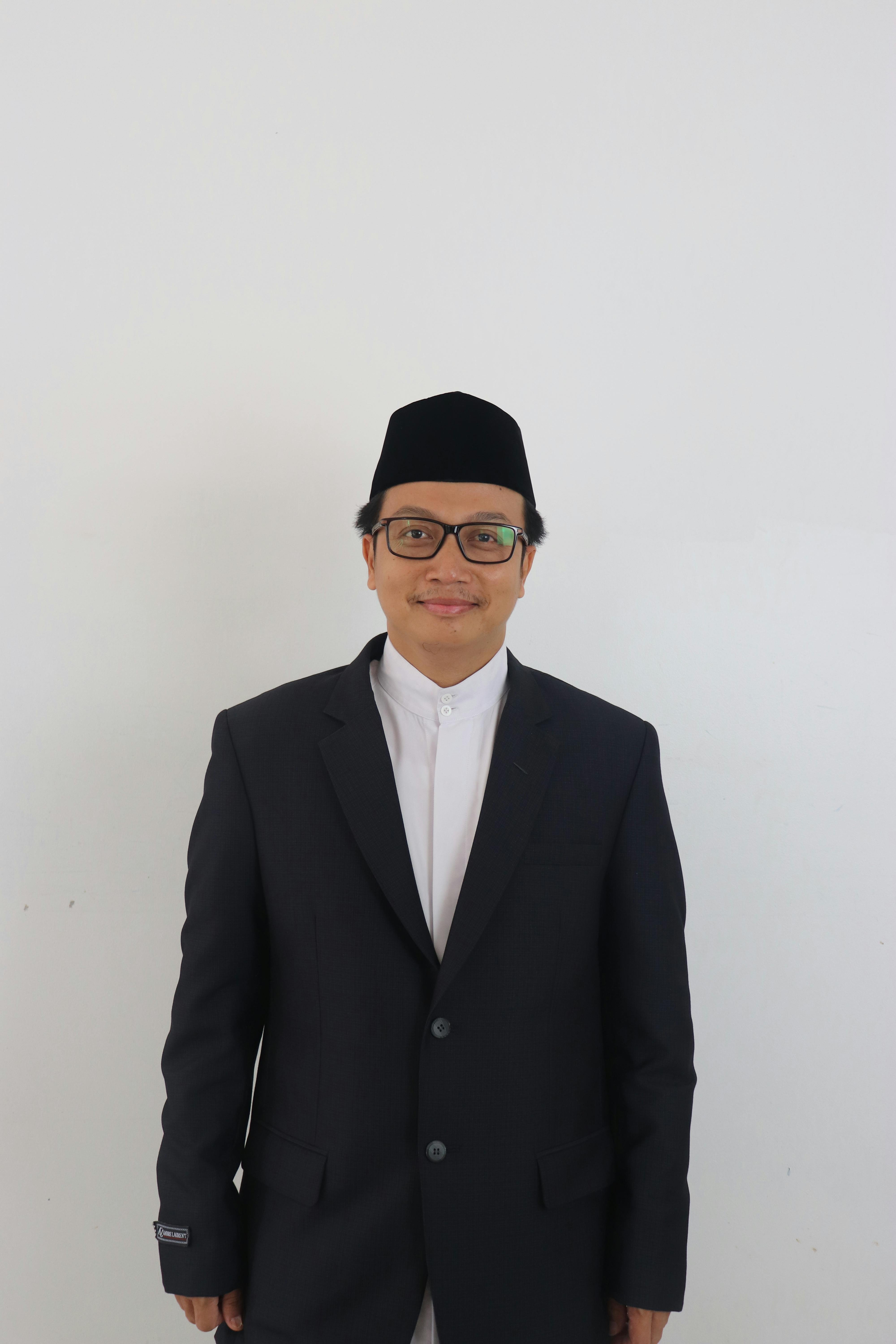 Portrait of a smiling man wearing a suit and kufi hat against a white background.